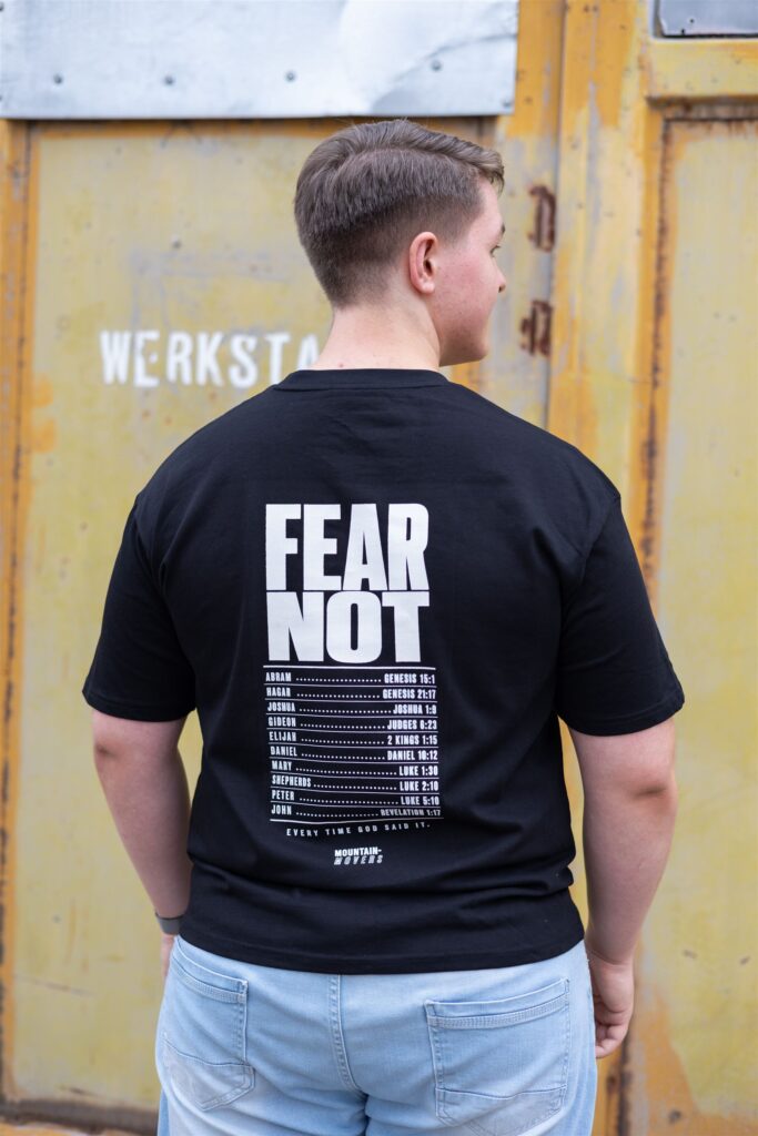 Mann trägt Mountain Movers Fear Not Shirt vor Industriekulisse – Produkt Shooting